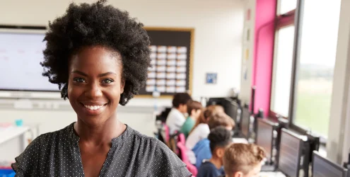 smiling teacher with students working at computers behind her