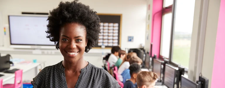 smiling teacher with students working at computers behind her