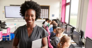 smiling teacher with students working at computers behind her