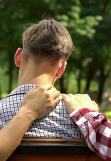 a teen and his parents sit on a park bench