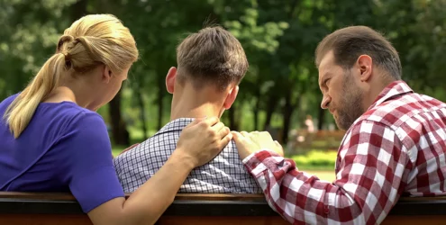 a teen and his parents sit on a park bench