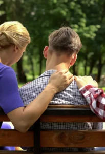 a teen and his parents sit on a park bench