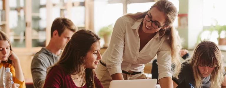 a smiling teacher helps students with their work