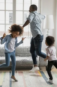 dad and two young kids dance around the living room