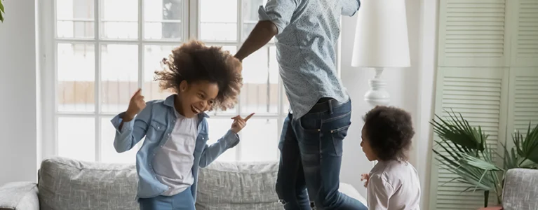 dad and two young kids dance around the living room