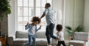 dad and two young kids dance around the living room
