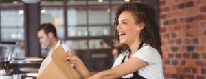 smiiling woman hands a bag of pastries to a customer