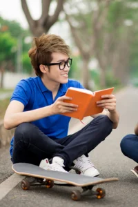 two teen boys reading books and talking on a sidewalk
