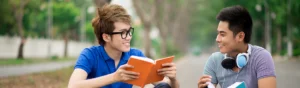 two teen boys reading books and talking on a sidewalk