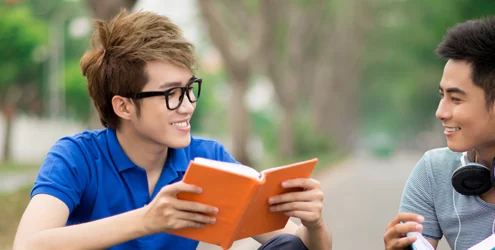 two teen boys reading books and talking on a sidewalk