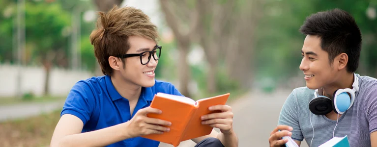 two teen boys reading books and talking on a sidewalk