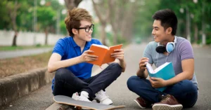 two teen boys reading books and talking on a sidewalk