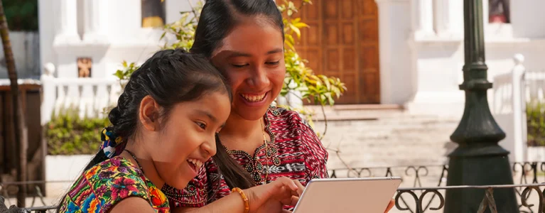 indigenous mother and daughter reading together in a courtyard