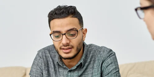 young man sitting on a couch talking to a counselor