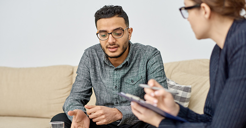 young man sitting on a couch talking to a counselor