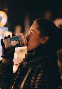 woman drinking coffee in front of holiday lights