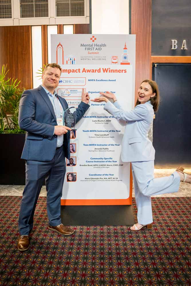 two people stand next to a sign listing award winners
