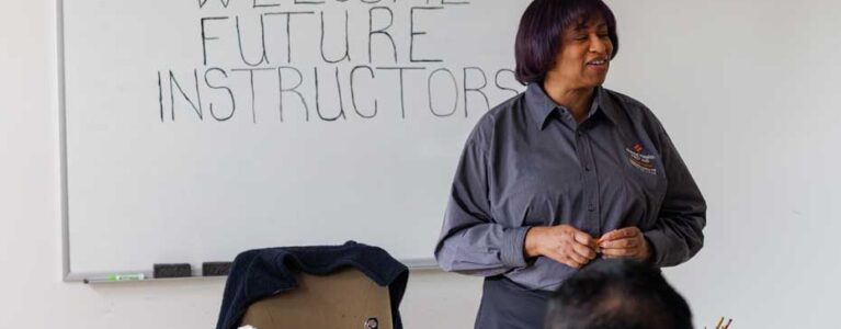 an instructor stands at the front of a classroom