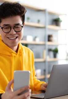 a man looks at his phone while using a computer