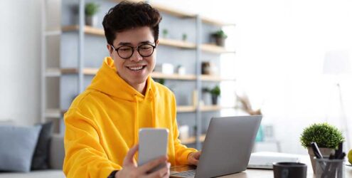a man looks at his phone while using a computer