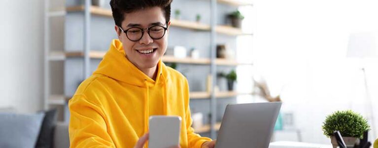 a man looks at his phone while using a computer