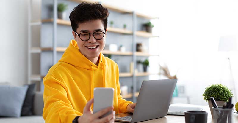 a man looks at his phone while using a computer