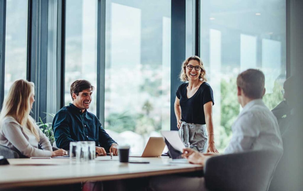 a group of people in a conference room, talking and smiling