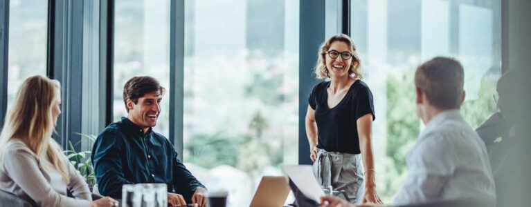 a group of people in a conference room, talking and smiling