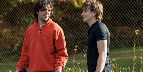 two men stand talking on a tennis court