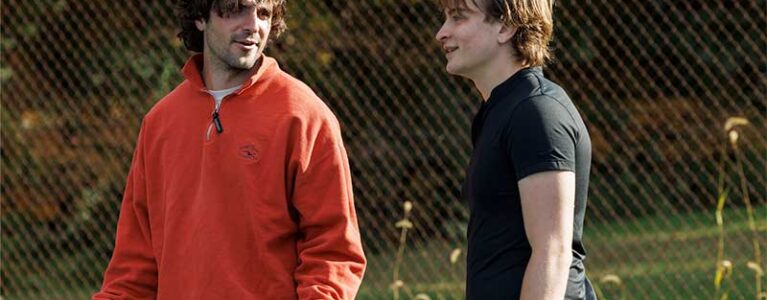 two men stand talking on a tennis court