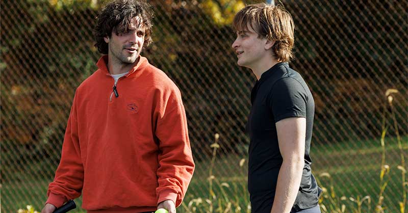 two men stand talking on a tennis court